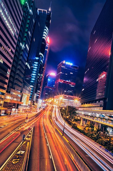 Street traffic in Hong Kong at night. Office skyscraper buildings and busy traffic on highway road with blurred cars light trails. Hong Kong