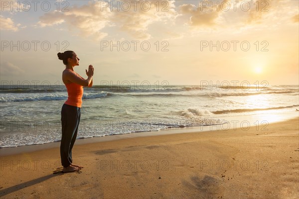 Woman doing Ashtanga Vinyasa Yoga asana Tadasana Samasthiti yoga posture on beach on sunset