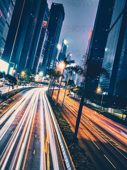 Street traffic in Hong Kong at night. Office skyscraper buildings and busy traffic on highway road with blurred cars light trails. Hong Kong