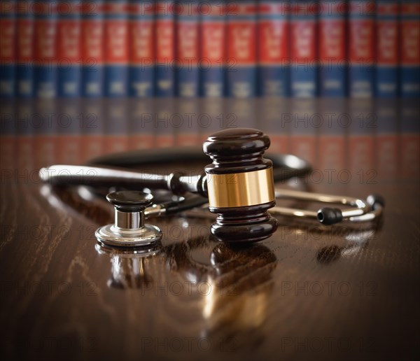 Gavel and stethoscope on wooden table with law books in background