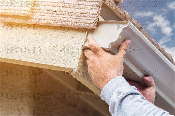 Worker attaching aluminum rain gutter to fascia of house