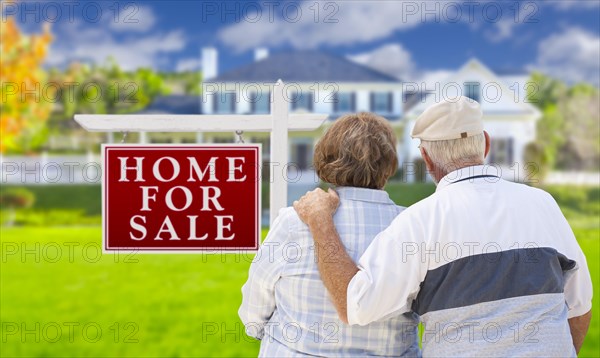 Happy senior couple front of for sale real estate sign and house