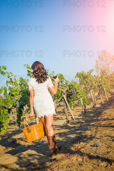 Beautiful young adult woman enjoying glass of wine tasting walking in the grape vineyard