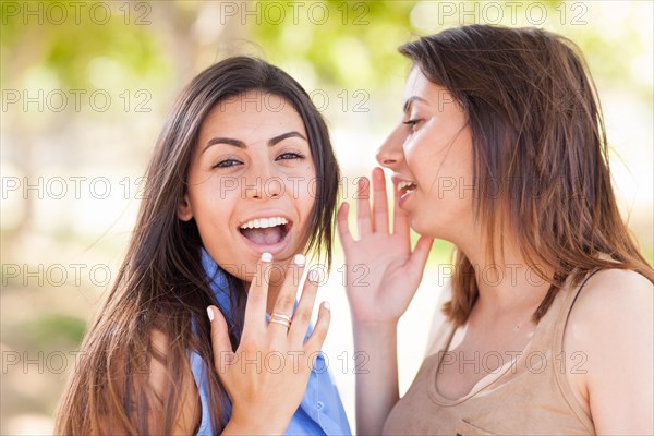 Two beautiful ethnic twin sisters whispering secrets outdoors