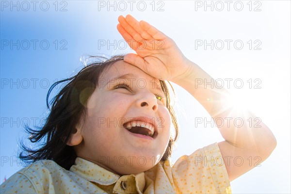 Happy boy in flare sunshine with hand at forehead