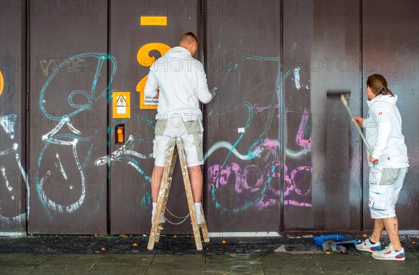 Two painters paint over graffiti on a building wall