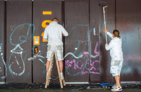 Two painters paint over graffiti on a building wall