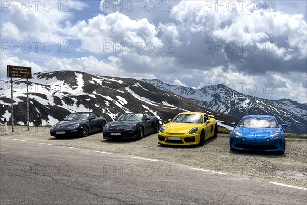 Porsche sports car and Renault Alpine standing at the top of mountain pass in Alps