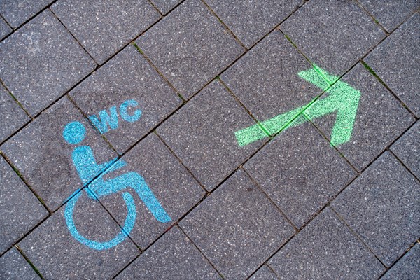 A green arrow with a blue pictogram for a wheelchair-accessible toilet points the way to a disabled toilet on the floor of the pedestrian zone