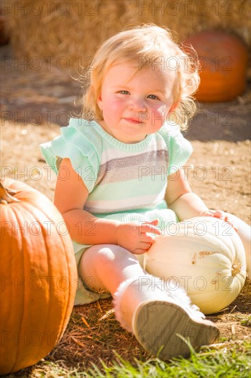 Adorable baby girl having fun in a rustic ranch setting at the pumpkin patch