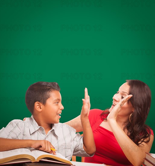 Blank chalk board behind hispanic young boy and famale adult studying