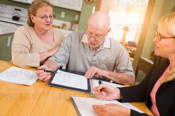 Senior adult couple going over documents in their home with agent at signing