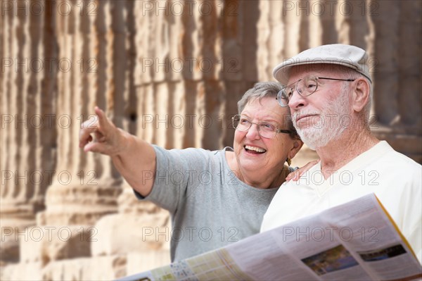 Happy senior adult couple tourists with brochure next to ancient column ruins