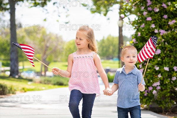 Young sister and brother waving american flags at the park