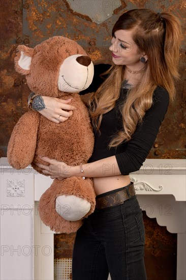 Portrait im Studio einer huebschen jungen Frau mit Tattoos und einem Halsband aus Leder und einem grossen Plueschtier im Arm. Die langen glatten braunen Haare sind zu einem Pferdeschwanz gebunden