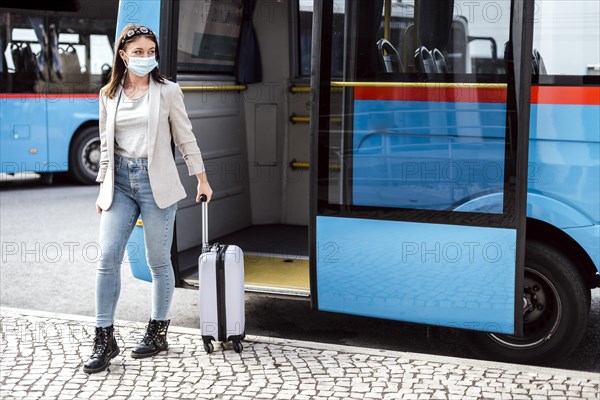 A young woman with mask and luggage has just left the bus after a long trip