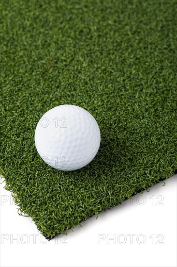 Golf ball resting on section of artificial turf grass on white background