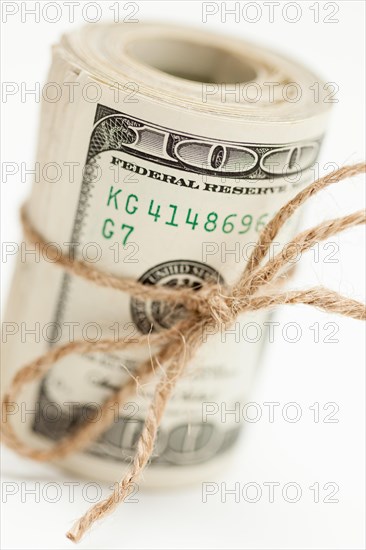 Roll of one hundred dollar bills tied in burlap string on white