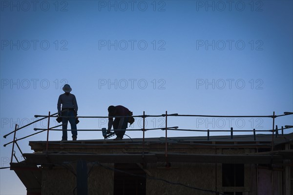 Construction workers silhouette on roof of building