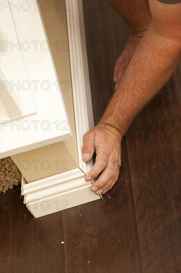 Contractor fitting new baseboard to wall and new laminate flooring abstract