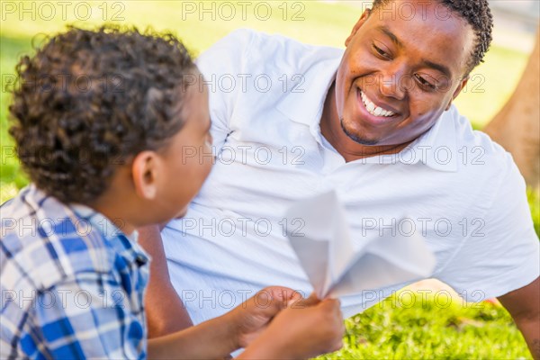 Happy african american father and mixed-race son playing with paper airplanes in the park