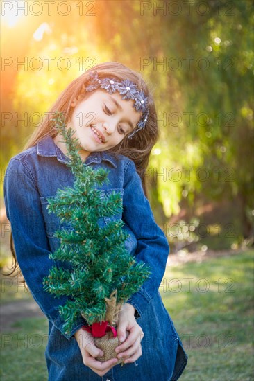 Cute mixed-race young girl holding small christmas tree outdoors