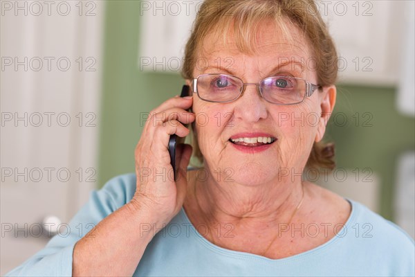 Happy senior adult woman on her smart cell phone in kitchen