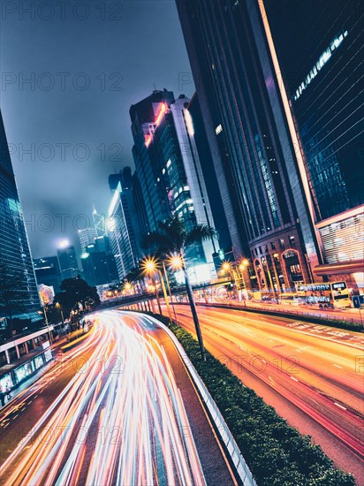 Street traffic in Hong Kong at night. Office skyscraper buildings and busy traffic on highway road with blurred cars light trails. Hong Kong