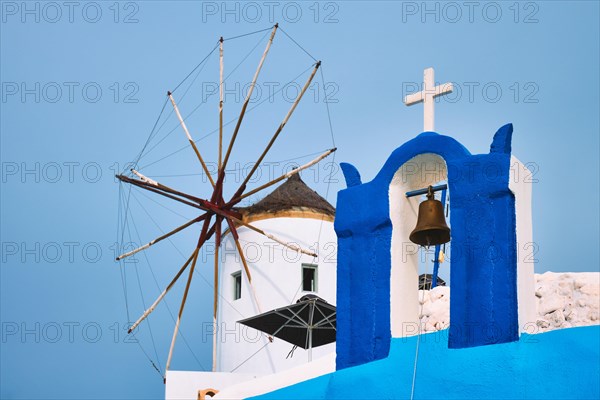 Old traditional whitewashed greek windmill and orthodox christian church bell on Santorini island in Oia town