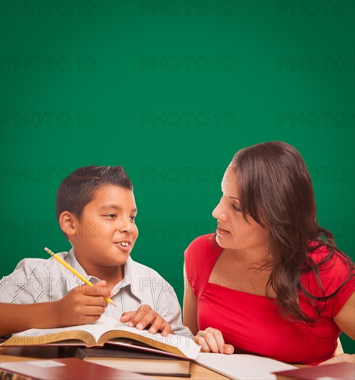 Blank chalk board behind hispanic young boy and famale adult studying