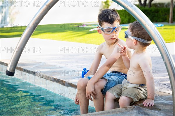 Young mixed-race chinese and caucasian brothers wearing swimming goggles playing at the pool