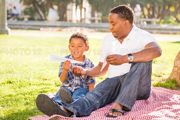 Happy african american father and mixed-race son playing with paper airplanes in the park