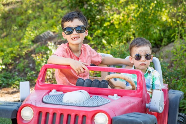 Young mixed-race chinese and caucasian brothers wearing sunglasses playing in toy car