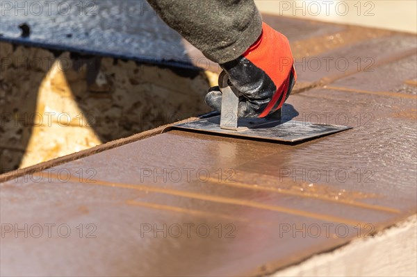 Construction worker using hand groover on wet cement forming coping around new pool