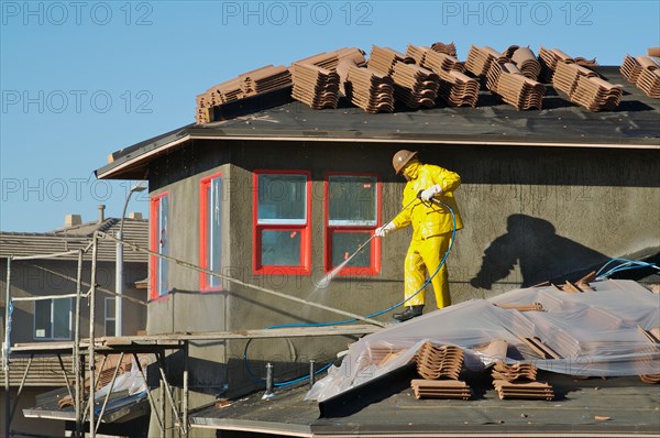 Construction worker pressure washes fresh applied surface of new home exterior