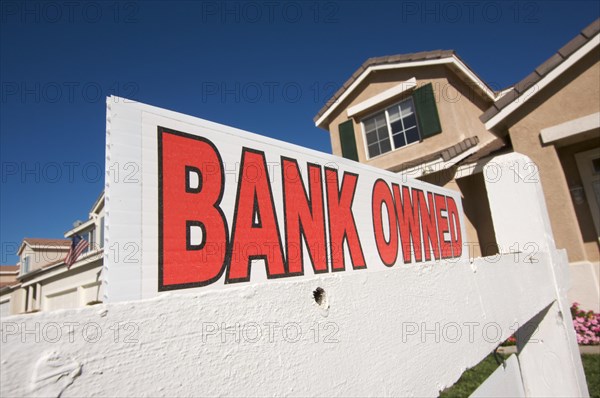 Bank owned real estate sign and house with american flag in the background