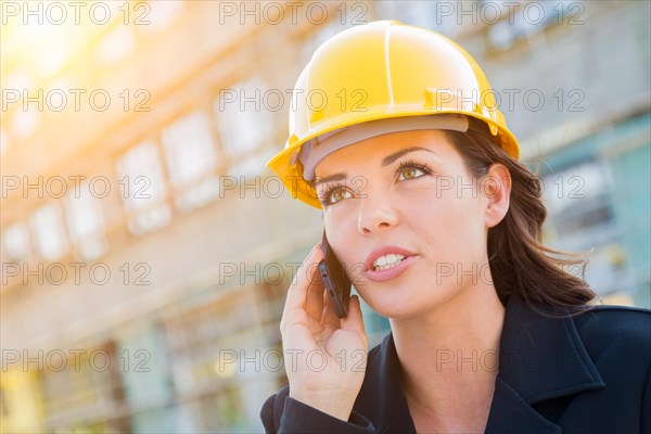 Young professional female contractor wearing hard hat at contruction site using cell phone