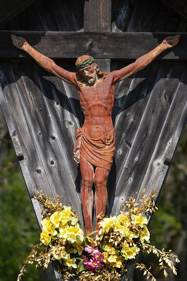 Geschnitztes Wegkreuz mit Blumenschmuck