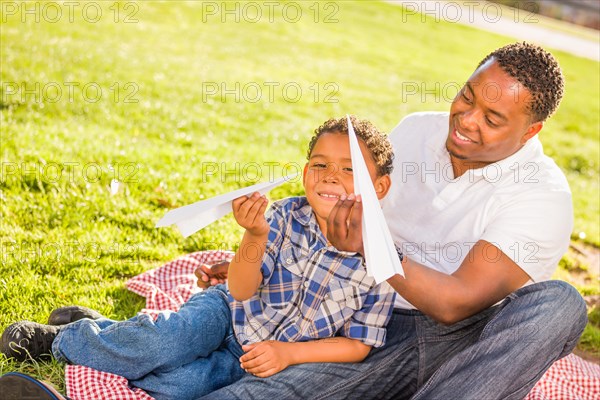 Happy african american father and mixed-race son playing with paper airplanes in the park