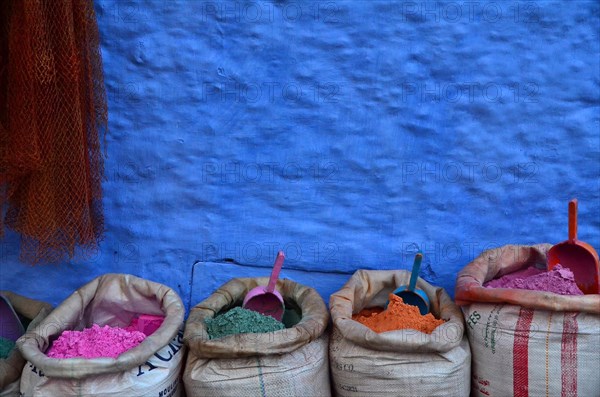 Colourful paint powder in bags in front of blue wall with shovel