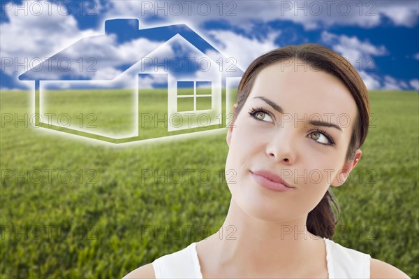 Contemplative woman in grass field looking up and over to the side with ghosted house figure behind