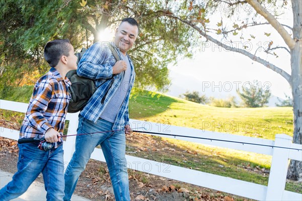 mixed-race father and son outdoors walking with fishing poles