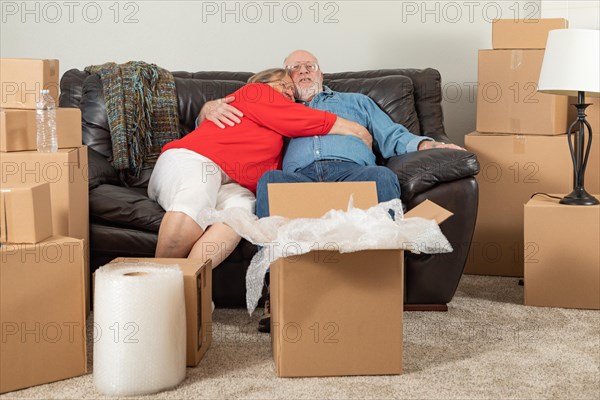 Affectionate tired senior adult couple resting on couch surrounded by moving boxes