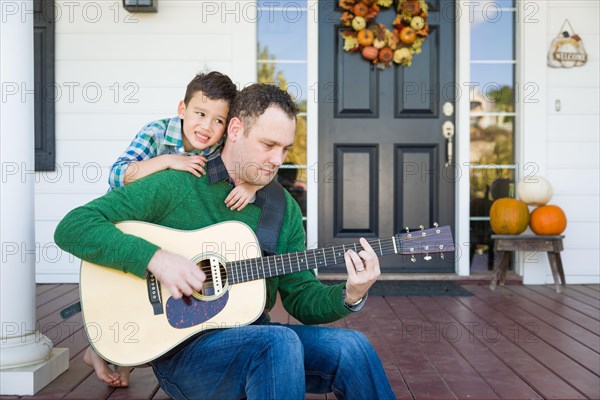 Young mixed-race chinese and caucasian son singing songs and playing guitar with father