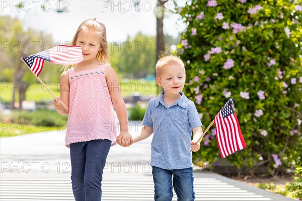 Young sister and brother waving american flags at the park