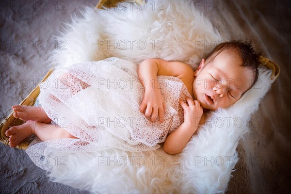 Cute newborn baby boy sleeping in the basket on fluffy blanket