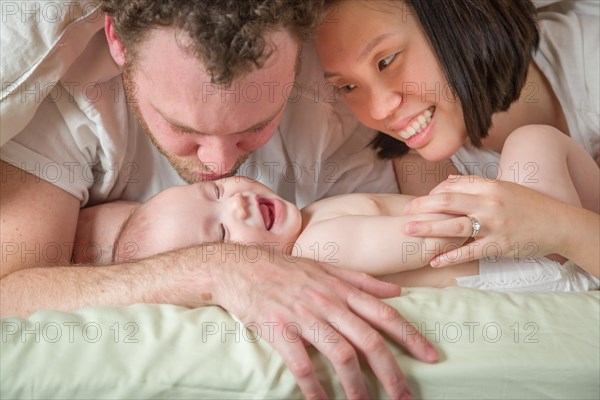 mixed-race chinese and caucasian baby boy laying in bed with his father and mother