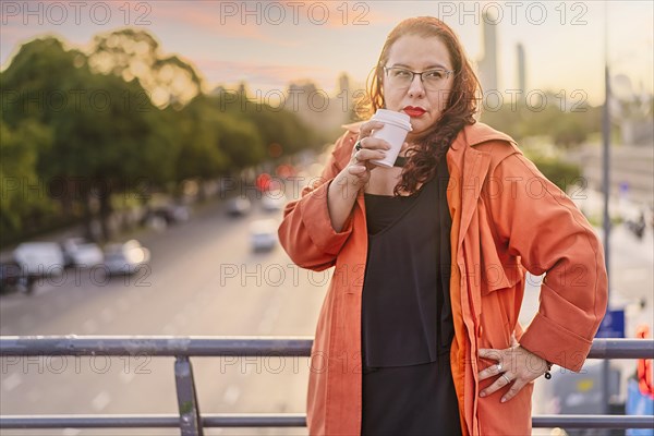 Woman standing on a bridge at sunset having a coffee