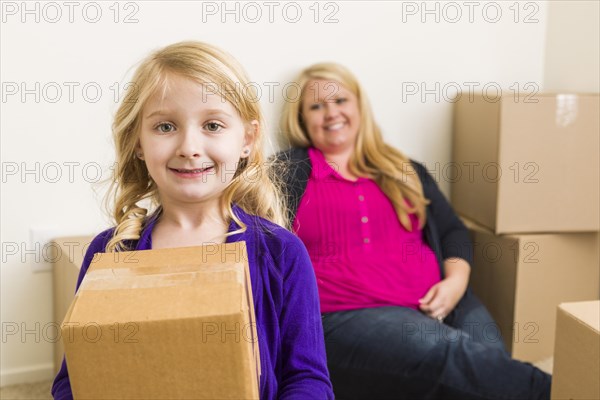 Happy young mother and daughter in empty room with moving boxes