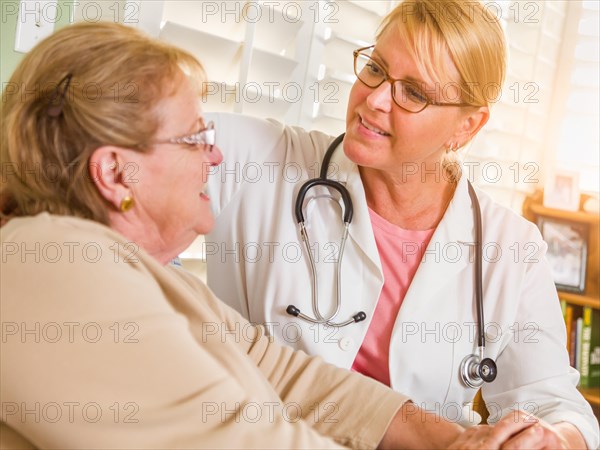 Happy smiling doctor or nurse talking to senior woman in chair at home